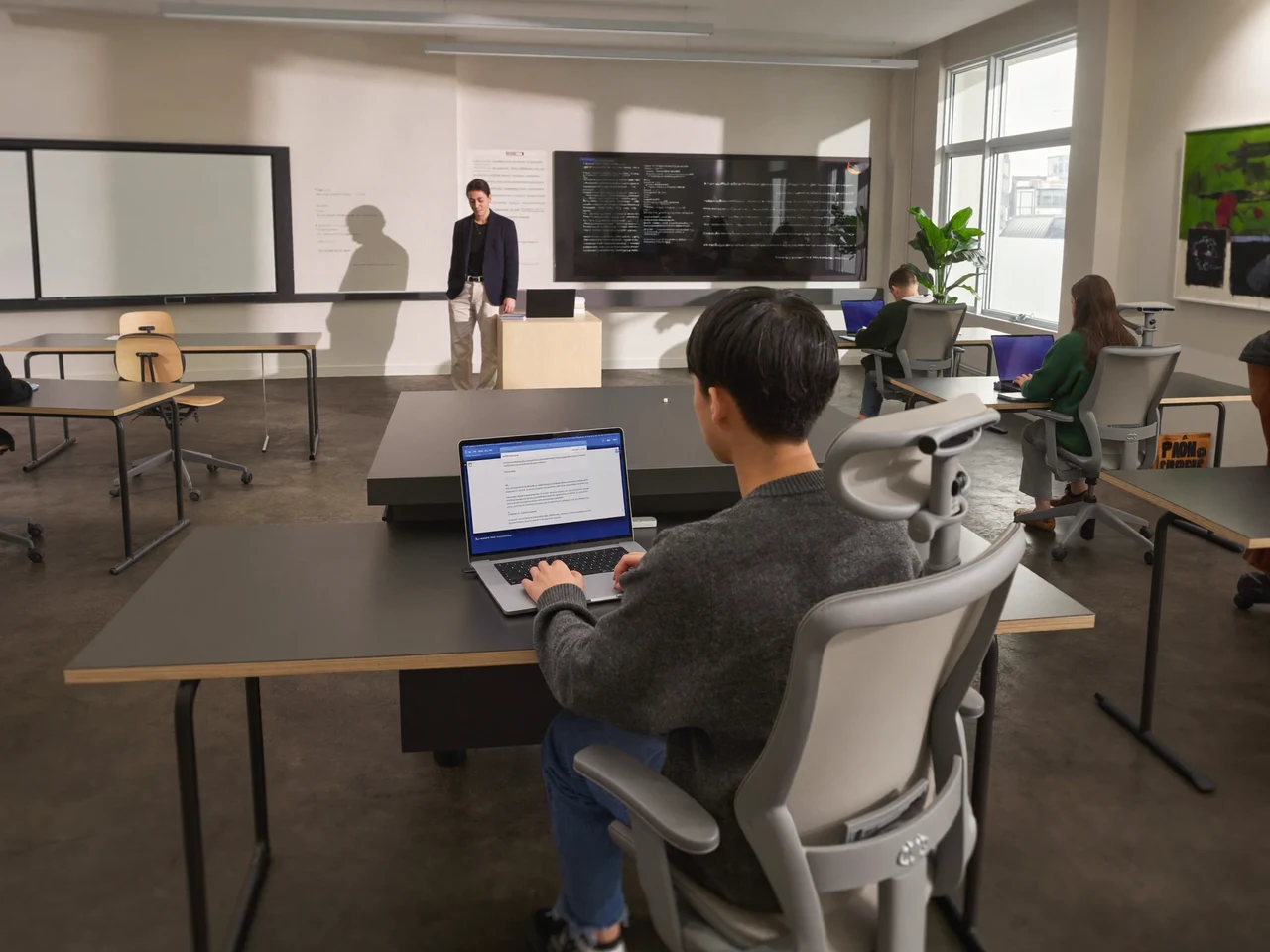 Aula luminosa con docente e studenti al lavoro su portatili
