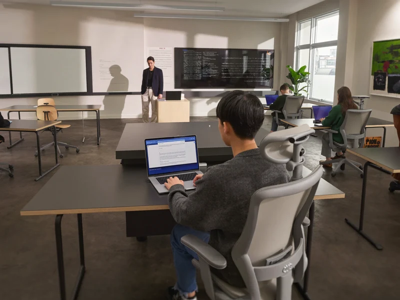 Aula luminosa con docente e studenti al lavoro su portatili